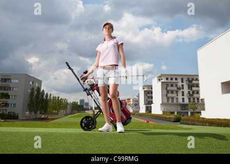 In Germania, in Baviera, Monaco di Baviera, giovane donna in piedi accanto al carrello da golf in città-campo da golf Foto Stock