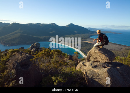 Un escursionista si affaccia su Wineglass Bay dalla cima di Mt Amos. Parco Nazionale di Freycinet, Tasmania, Australia Foto Stock