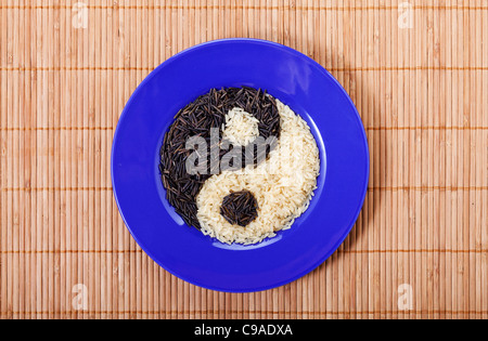 In bianco e nero il riso in un blu scuro piastra in forma di Oriente simbolo Yin e yang, su un tappetino Foto Stock