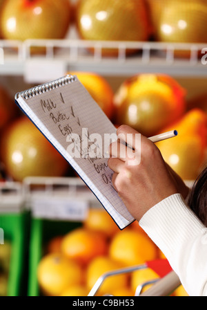 Immagine di mani femminili con penna azienda elenco prodotti mentre acquistare merci in un supermercato Foto Stock