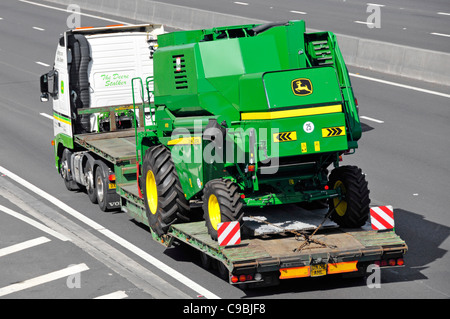 Macchine agricole prodotto dalla John Deere hgv autocarro articolato e caricatore basso il trasporto di una mietitrebbia John Deere Harvester macchina Autostrada Essex Inghilterra Foto Stock