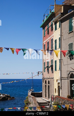 L'Italia, Liguria, Riomaggiore Cinque Terre, la vista del villaggio di edifici con bunting e mare in background Foto Stock