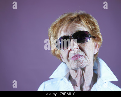 Senior donna con occhiali da sole contro sfondo viola Foto Stock