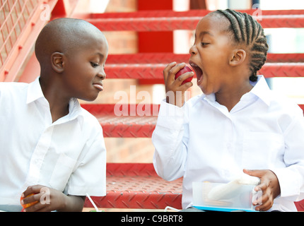 Un ragazzo e una ragazza mangiare apple sui passi al di fuori della scuola, Johannesburg, provincia di Gauteng, Sud Africa Foto Stock