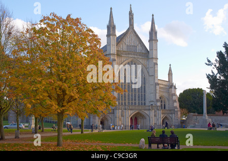 Fronte ovest della cattedrale di Winchester in novembre al sole con bronzo-lasciato tree e le persone che si godono la unseasonable meteo. Foto Stock