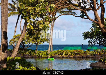 Kauai, Hawaii, donna galleggianti in stagno tranquilla accanto alla spiaggia Foto Stock