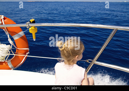 La bionda bambina vista posteriore la vela in barca nel blu del Mare di Ibiza Foto Stock