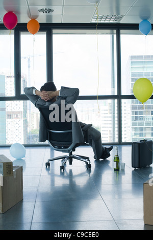 Imprenditore seduto in un nuovo ufficio con palloncini e scatole Foto Stock