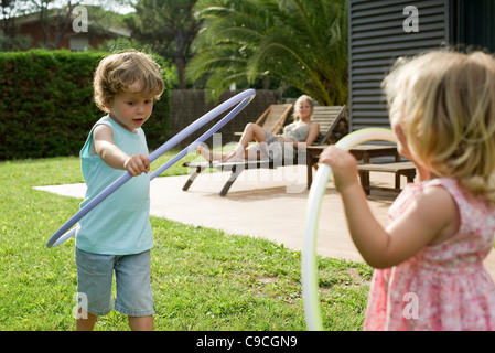 Bambini che giocano con rollbar di plastica mentre la Madre veglia in background Foto Stock