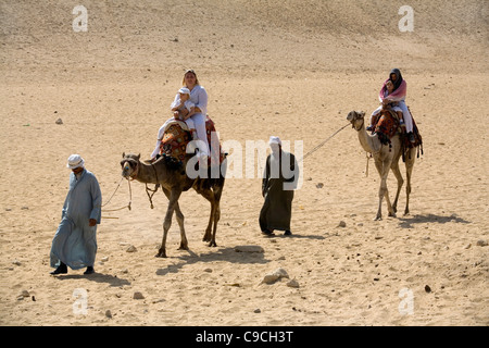 Beduins cavalcare i turisti sui cammelli nel deserto intorno alle piramidi di Giza, il Cairo, Egitto Foto Stock