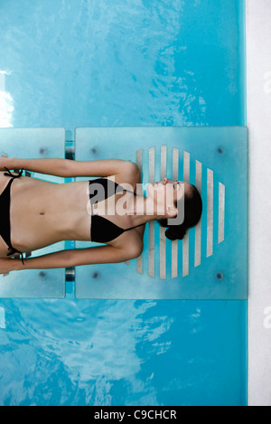 Giovane donna a prendere il sole in piscina Foto Stock