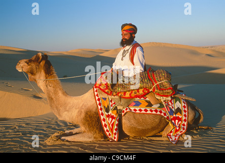 Signor deserto in tradizionale Rajput, Rajasthani, in piedi accanto a un cammello sulle dune di sabbia vicino a Jaisalmer, Rajasthan, India Foto Stock