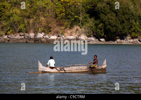 Due giovani ragazzi 8-11 anni paddle loro outrigger piroga off Mamoko isola, Madagascar. La foresta tropicale in background. Foto Stock