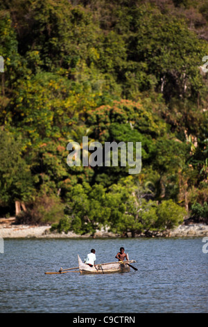 Due giovani ragazzi 8-11 anni paddle loro outrigger piroga off Mamoko isola, Madagascar. La foresta tropicale in background. Foto Stock