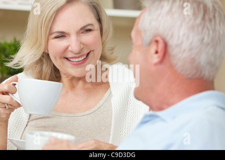 Felice senior l uomo e la donna giovane seduti insieme a casa sorridenti e bere il tè o caffè Foto Stock