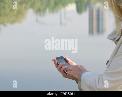 L'Italia, Piemonte, Close-up di donna l'invio di messaggi di testo dalla riflessione sul fiume Foto Stock