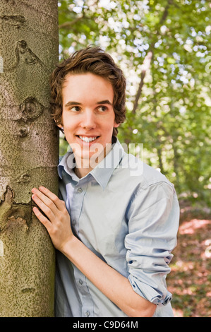 Giovane uomo in piedi da un albero nel bosco Foto Stock