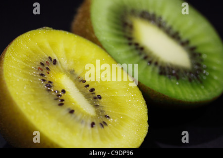 Un vivace duo di kiwi dorati e verdi, tagliati a fette per rivelare i loro succosi centri polpati di semi su un elegante sfondo scuro. Foto Stock