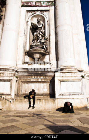 Venezia Italia. Una donna sulle sue ginocchia mendica per denaro come un giovane uomo legge un libro al di fuori della chiesa di Santa Maria del Rosario sul Canale della Giudecca Foto Stock