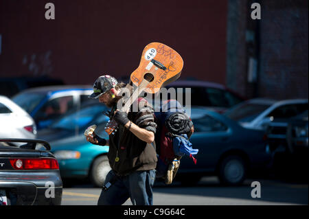 3 agosto 2011 - Portland, Oregon, Stati Uniti - un senzatetto uomo mangia una ciambella come egli cammina per le strade del centro cittadino di Portland, Oregon cercando un posto per giocare la sua chitarra. Senzatetto i musicisti spesso di soddisfare le loro esigenze di base mediante la riproduzione sulla strada per le donazioni. Portland ospita una grande popolazione di sfollati p Foto Stock