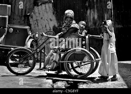 Sett. 27, 2010 - Kano, Kano, NIGERIA - una donna afflitta con la polio che non ha dato il suo nome, porta il suo bambino mentre la sua giovane figlia spinge il suo intorno sulla sua mano sedia a rotelle a gomito. Nonostante la presenza di lei e tre altri vicini storpio con la poliomielite, la maggior parte delle persone nella zona rifiutano ancora p Foto Stock