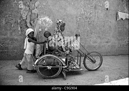 Sett. 27, 2010 - Kano, Kano, NIGERIA - una donna afflitta con la polio che non ha dato il suo nome, porta il suo bambino mentre la sua giovane figlia spinge il suo intorno sulla sua mano sedia a rotelle a gomito. Nonostante la presenza di lei e tre altri vicini storpio con la poliomielite, la maggior parte delle persone nella zona rifiutano ancora p Foto Stock