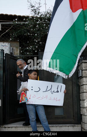 Un ragazzo palestinese ha un segno in arabo come un colono ebraico lascia una casa, che è stata occupata dai coloni ebrei durante una manifestazione contro l'attività di insediamento a Sheikh Jarrah, un quartiere prevalentemente palestinese il 23 aprile 2011, a Gerusalemme Est, Israele. Il quartiere palestinese di Sheikh Jarrah è attualmente il centro di una serie di controversie sulla proprietà tra palestinesi e israeliani. Alcune case sono state occupate dai coloni israeliani a seguito di una sentenza della Corte. Foto Stock