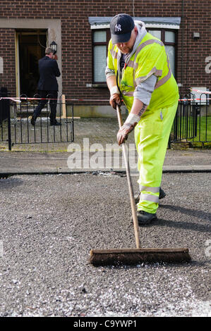 Belfast, Regno Unito. 10 mar 2012. Un lavoratore del consiglio vetro pennelli di una strada dopo un attentato alla bomba in una casa Foto Stock