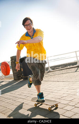 Un giovane uomo di skateboard sul lungomare a Aberystwyth Wales UK, 26 marzo 2012: popolazione gode di un clima eccezionalmente caldo al mare. Tutto il Regno Unito è crogiolarsi in temperature più tipica della fine di giugno. Foto Stock