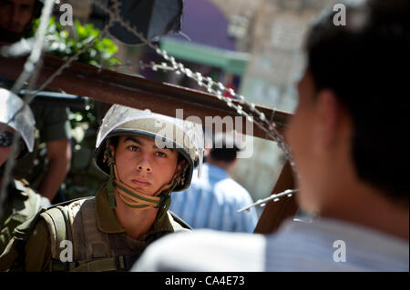 HEBRON, Territori palestinesi - Giugno 5, 2012: un soldato israeliano e la gioventù palestinese guarda ogni altro attraverso il filo spinato barricate durante la manifestazione nonviolenta che commemora la Naksa Day, l'anniversario dell'occupazione israeliana dei territori palestinesi nel 1967. Foto Stock