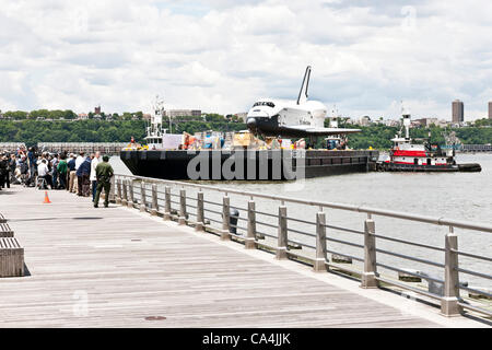 I membri dei media della rampa della folla di Pier 84 come rimorchiatore manovre chiatte che trasportano lo space shuttle Enterprise in posizione per il trasferimento da una gru a ponte di volo di Intrepid Sea Air & Space Museum di New York City. La navetta sarà aperto al pubblico il 19 luglio 2012. Foto Stock