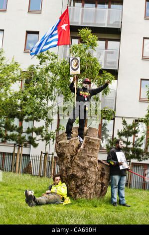 London, Regno Unito - 15 Giugno 2012: un manifestante detiene il Papua Occidentale bandiera mentre un uomo riposa in Altab Ali Park durante il carnevale di sporcizia. Più di 30 gruppi di attivisti da Londra e da tutto il mondo sono venuti insieme per evidenziare il traffico illecito di opere di estrazione mineraria e le aziende di estrazione. Foto Stock