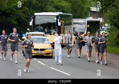 Sean Lewis età 16 da Llanbradach carryng la fiamma durante la fiaccola del relè per le Olimpiadi di Londra 2012 attraverso Abergavenny con polizia fiancheggianti security guide e gli autobus olimpico, Wales, Regno Unito Venerdì 25 Maggio 2012 Foto Stock