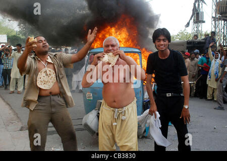 I membri di tutto il Pakistan Associazione GNC raccogliere vicino a bruciare auto-rickshaw chant slogan contro il carico di gas-spargimento durante la manifestazione di protesta a nord di sui gas company con sede a Lahore Lunedì, 28 maggio 2012. Foto Stock