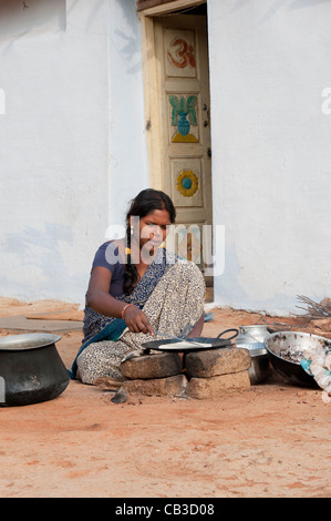 Giovani indiani moglie in un villaggio rurale facendo chapati su un fuoco aperto al di fuori di casa sua. Andhra Pradesh, India Foto Stock