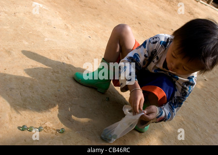 Un giovane ragazzo sta giocando con marmi su una strada di sporcizia in un Burmese Karen Paduang Refugee Camp di Mae Hong Son Provincia, Thailandia. Foto Stock