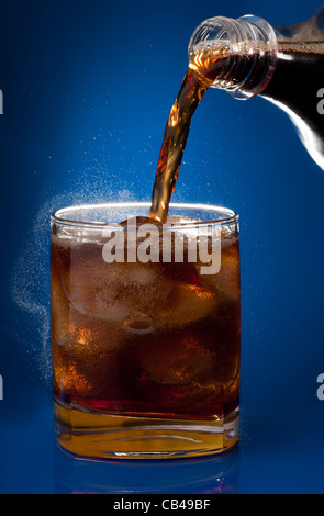 La classe con il freddo di cola e riempito di ghiaccio dalla bottiglia su sfondo blu Foto Stock