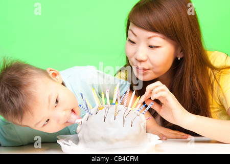 Ragazzo lambisce la sua torta di compleanno con la madre nelle vicinanze e un sacco di candele in esso Foto Stock