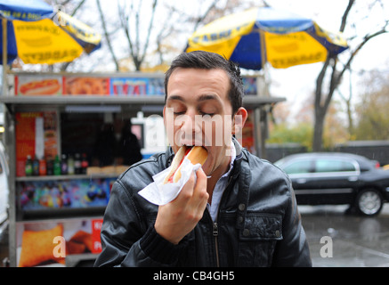 Giovane uomo di mangiare un hot dog con salsa di pomodoro e senape hanno acquistato dalla bancarella di strada Manhattan New York New York STATI UNITI D'AMERICA America Foto Stock