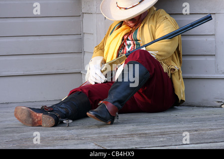 Un cowboy southwestern in appoggio contro un vecchio edificio con un fucile Foto Stock
