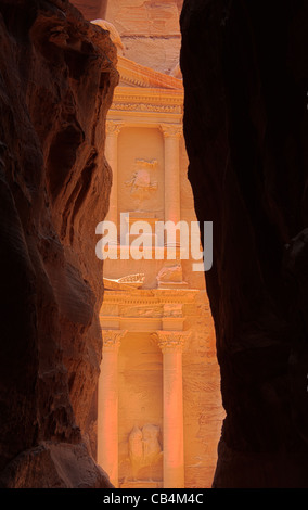 Primo assaggio del famoso edificio del Tesoro dalla stretta Siq ingresso canyon immerso nel rosso sole di mattina a Petra Foto Stock