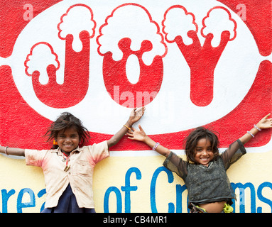 Sorridendo felice povero indiano mendicante nomade le ragazze in piedi di fronte a una gioia murale su una parete. Andhra Pradesh, India Foto Stock