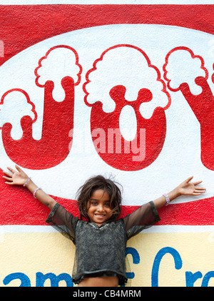 Sorridendo felice povero indiano mendicante nomadi ragazza in piedi di fronte a una gioia murale su una parete. Andhra Pradesh, India Foto Stock