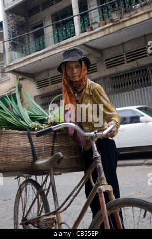 Una donna è la vendita di verdura verde da un cestello legata a una bicicletta su una strada di città di Battambang, Cambogia. Foto Stock