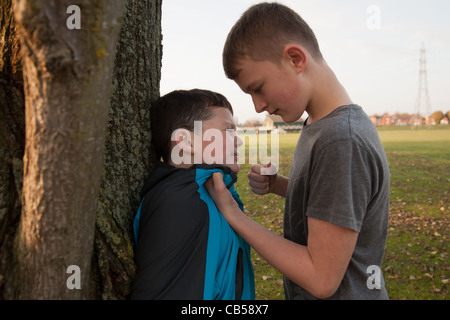 Un vecchio ragazzo bullismo un giovane ragazzo con il suo pugno azienda ribattuto lui fino contro un albero. Foto Stock