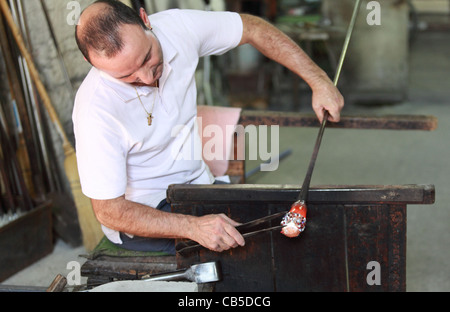 Un artigiano in una fabbrica di Murano lavora sulla produzione di un pezzo di vetro decorativo Foto Stock