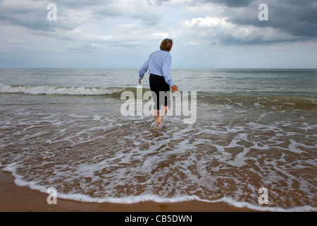 Uomo che indossa arrotolato tuta pantaloni a piedi in mare. Foto Stock