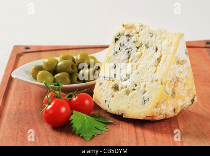 Cuneo di formaggio blu e una ciotola di olive sul bordo di taglio Foto Stock