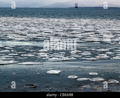 Grandi pezzi di ghiaccio galleggiante in acqua blu di un Alaskan Bay con un jack-up olio impianto di perforazione in background. Foto Stock