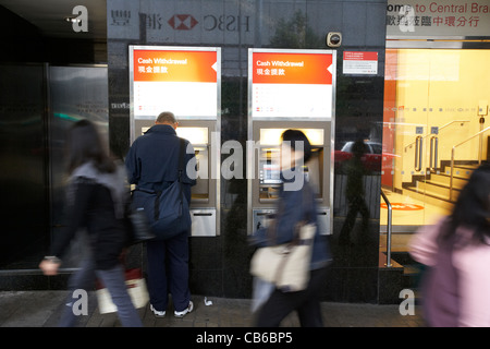 Uomo cinese tramite bancomat ATM in filiale di banca come la gente a piedi passato per il distretto centrale, isola di Hong kong, RAS di Hong Kong, Cina Foto Stock